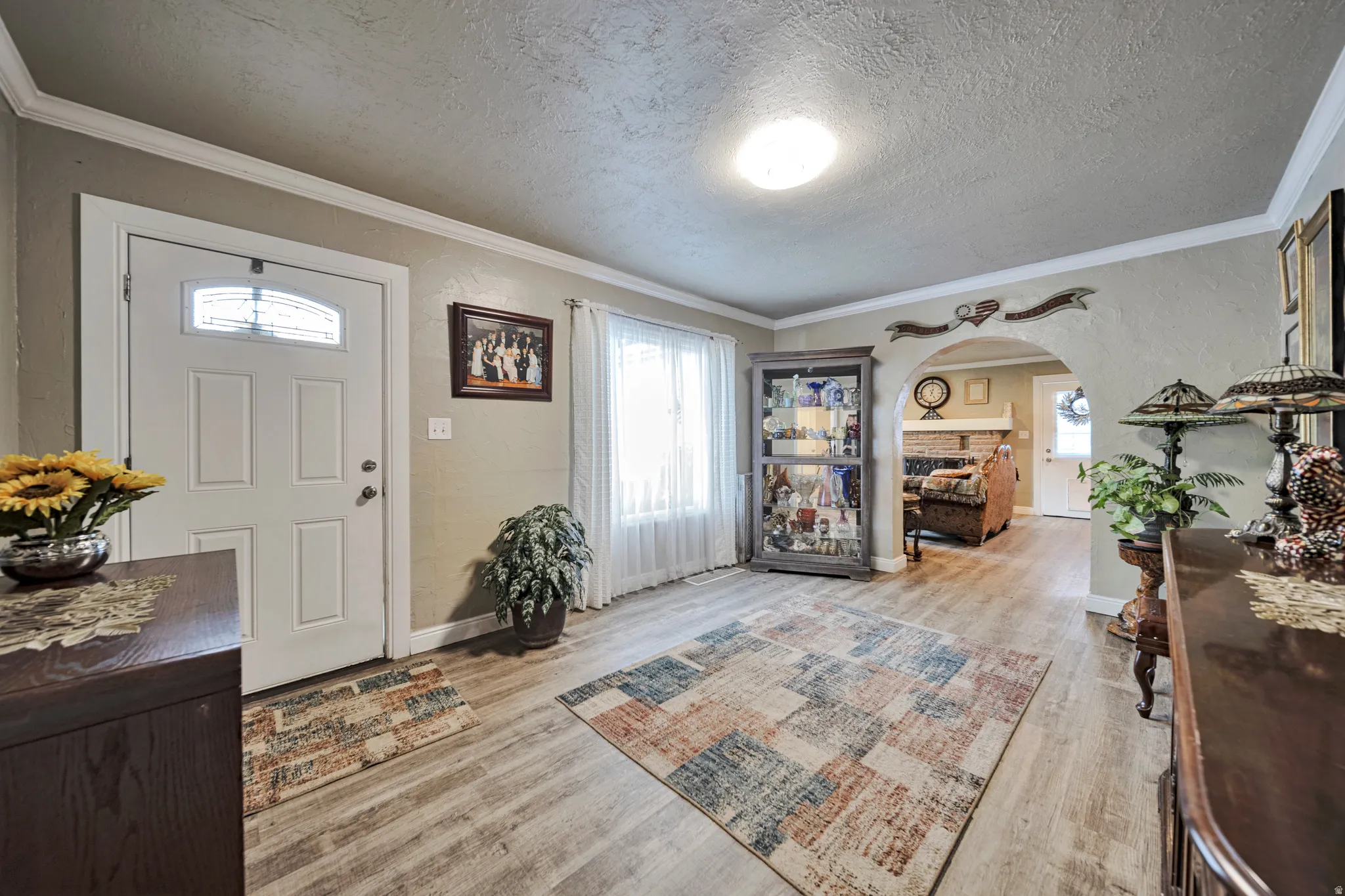 Inviting entryway featuring wood-finish flooring, white paneled entry door with decorative glass insert, and crown molding