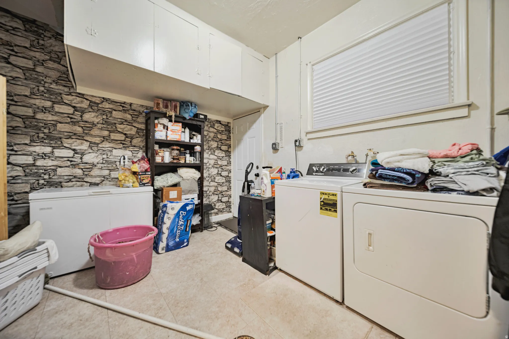 Functional utility space featuring a laundry area with appliances, extensive built-in overhead cabinetry, and a window with blinds