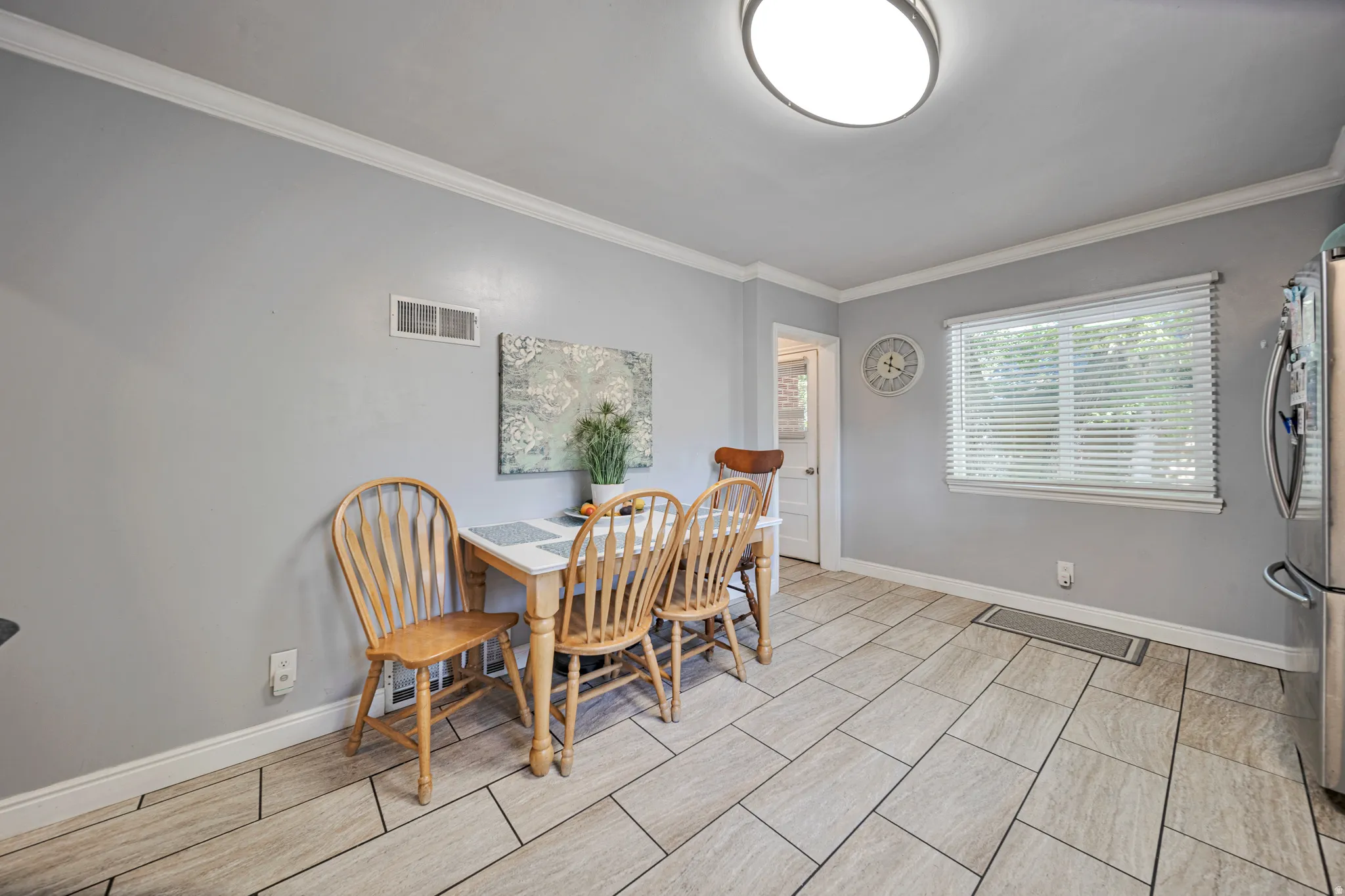 Dining area featuring rectangular tile flooring, crown molding, a flush-mount ceiling light, and a window with blinds