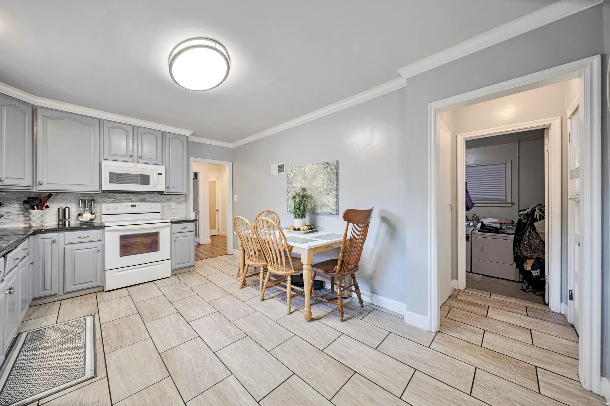 Kitchen featuring light gray cabinetry, dark countertops, white appliances, and a mosaic tile backsplash