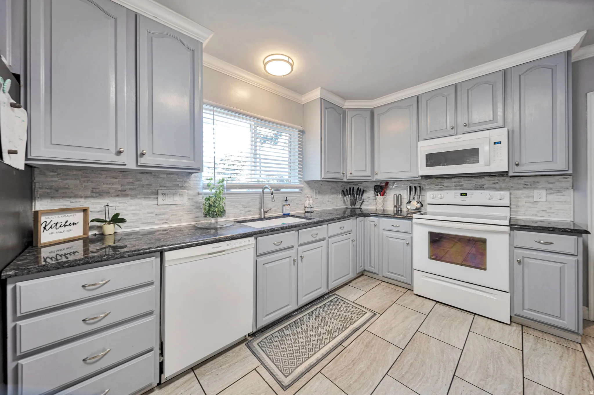 Kitchen featuring light gray cabinetry with crown molding, dark stone countertops, and a white tile backsplash