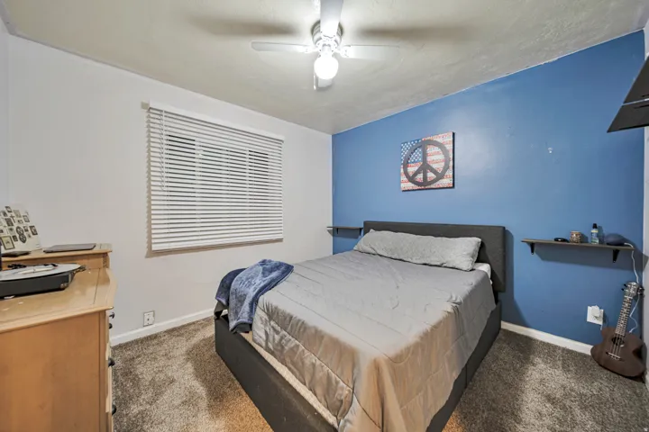 Carpeted room featuring a ceiling fan with integrated lighting, a window with horizontal blinds, and a contrasting accent wall