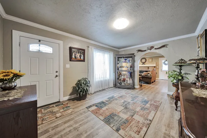 Inviting entryway featuring wood-finish flooring, white paneled entry door with decorative glass insert, and crown molding
