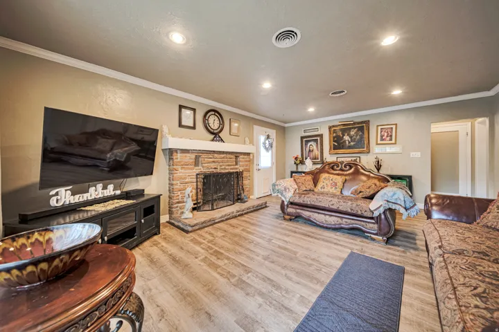 Living area featuring wood-finish flooring, a stone fireplace with hearth, crown molding, and recessed lighting