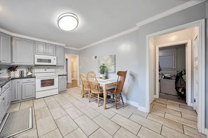 Kitchen featuring light gray cabinetry, dark countertops, white appliances, and a mosaic tile backsplash