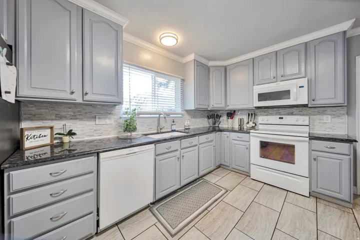 Kitchen featuring light gray cabinetry with crown molding, dark stone countertops, and a white tile backsplash