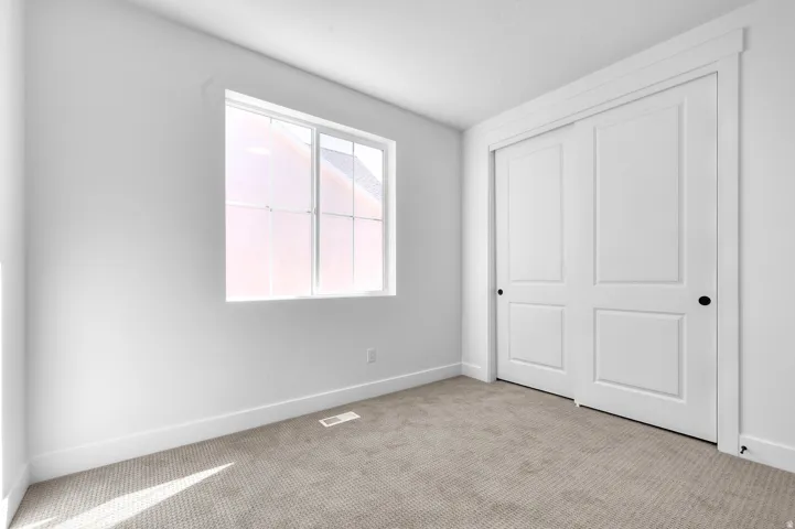 Window with grid pattern, neutral carpet, white walls, and built-in sliding closet doors with matte black hardware