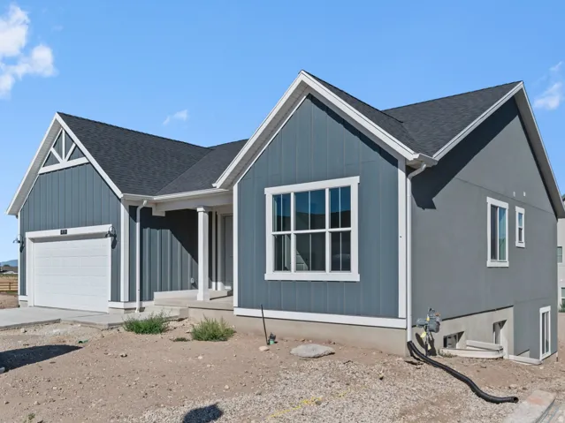 Modern exterior featuring a prominent front window, attached garage, covered entryway with columns, and a basement access door