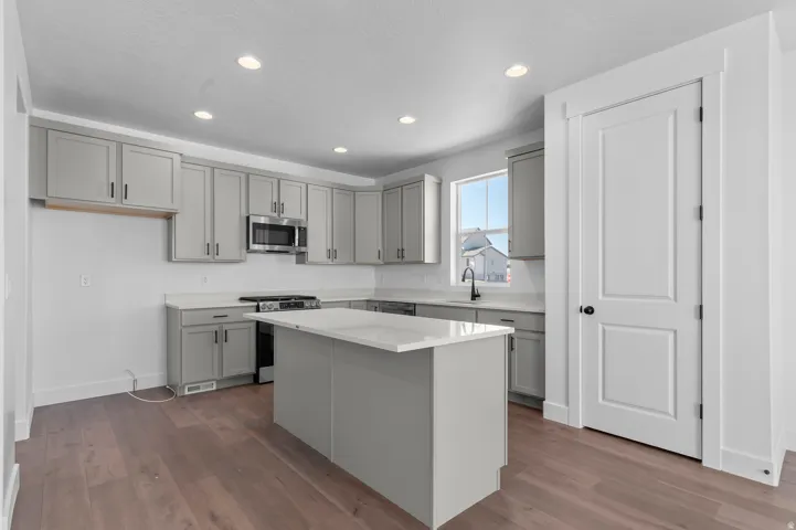 Kitchen featuring an island, light gray cabinetry, built-in microwave, stainless steel sink with a black faucet, and wood-finish flooring