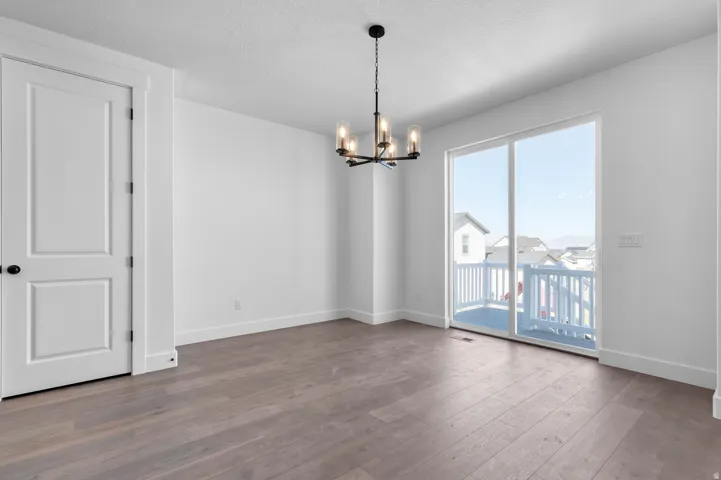 Wood-finish flooring, white walls, black-finish chandelier, two-panel interior door, and a sliding glass door opening to an outdoor deck with white railing