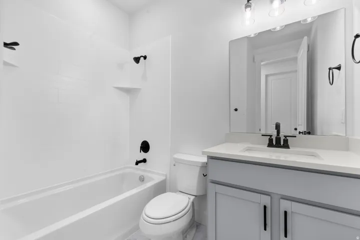 White tiled tub/shower combination, light gray vanity with white countertop, undermount sink, and matte black fixtures