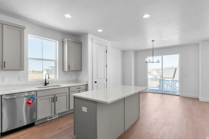Kitchen featuring an island, light gray cabinetry, white countertops, wood-finish flooring, and a stainless steel dishwasher