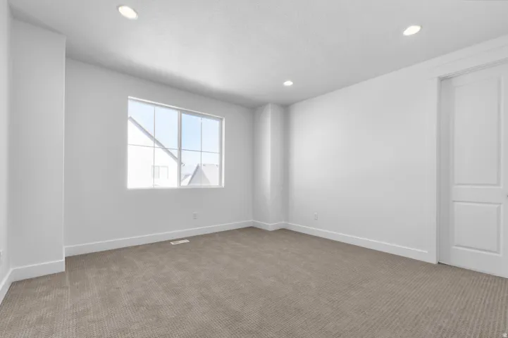 Recessed ceiling lights illuminate this room featuring wall-to-wall carpeting, white walls, and a multi-pane window