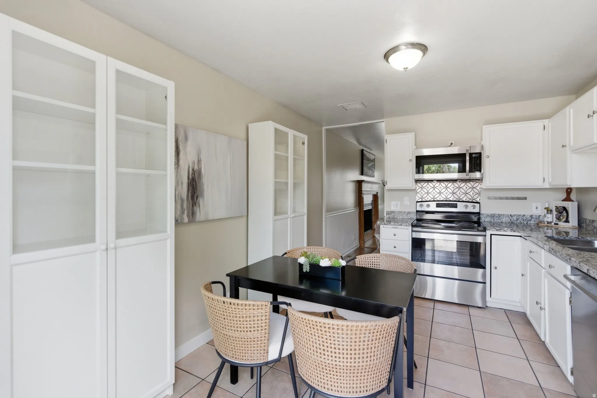 Kitchen dining area featuring white cabinetry, light-toned tiled flooring, and granite-style countertops