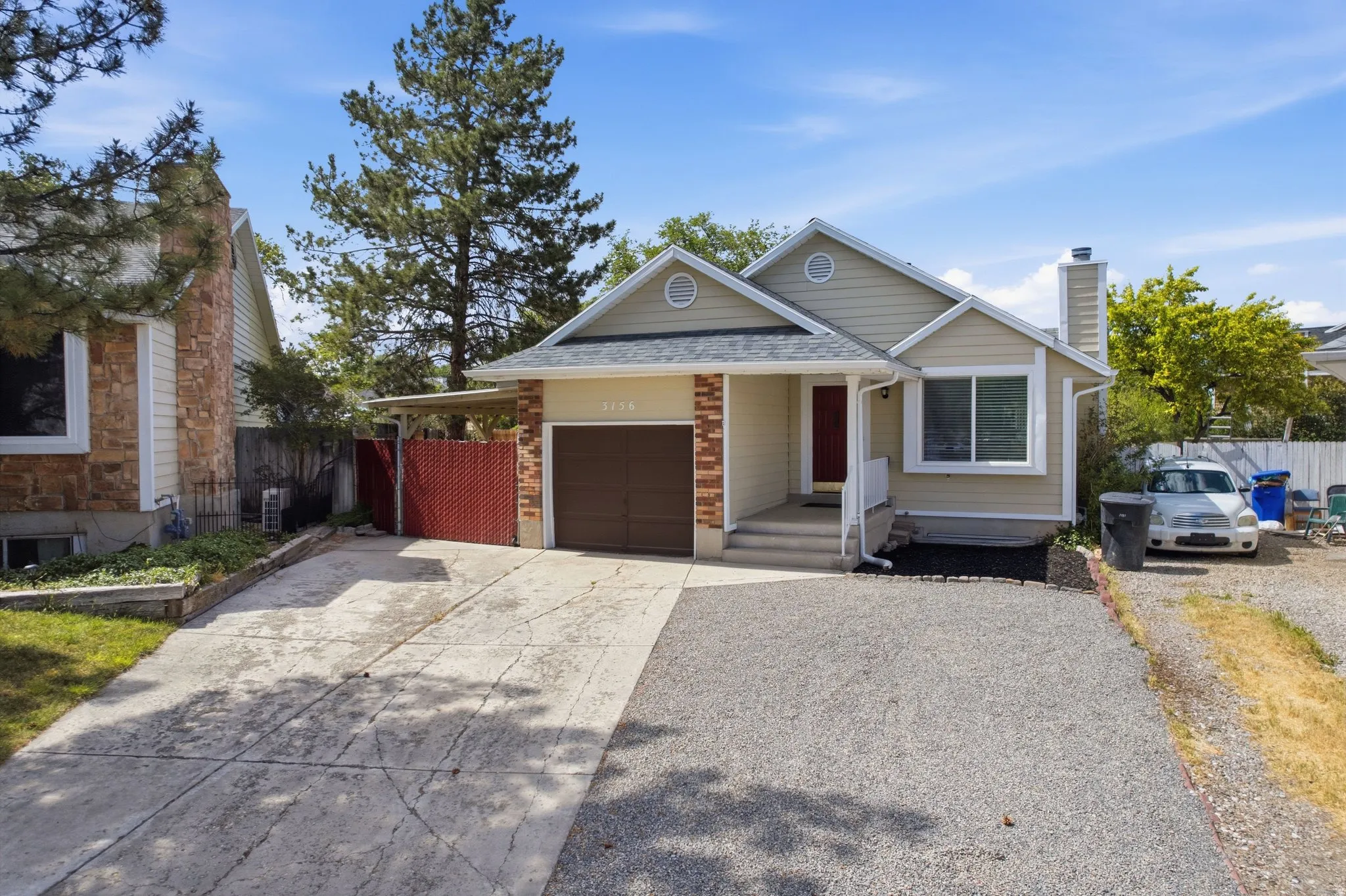 Property exterior featuring a light beige siding, an attached garage, a red front door, and a partially covered concrete driveway