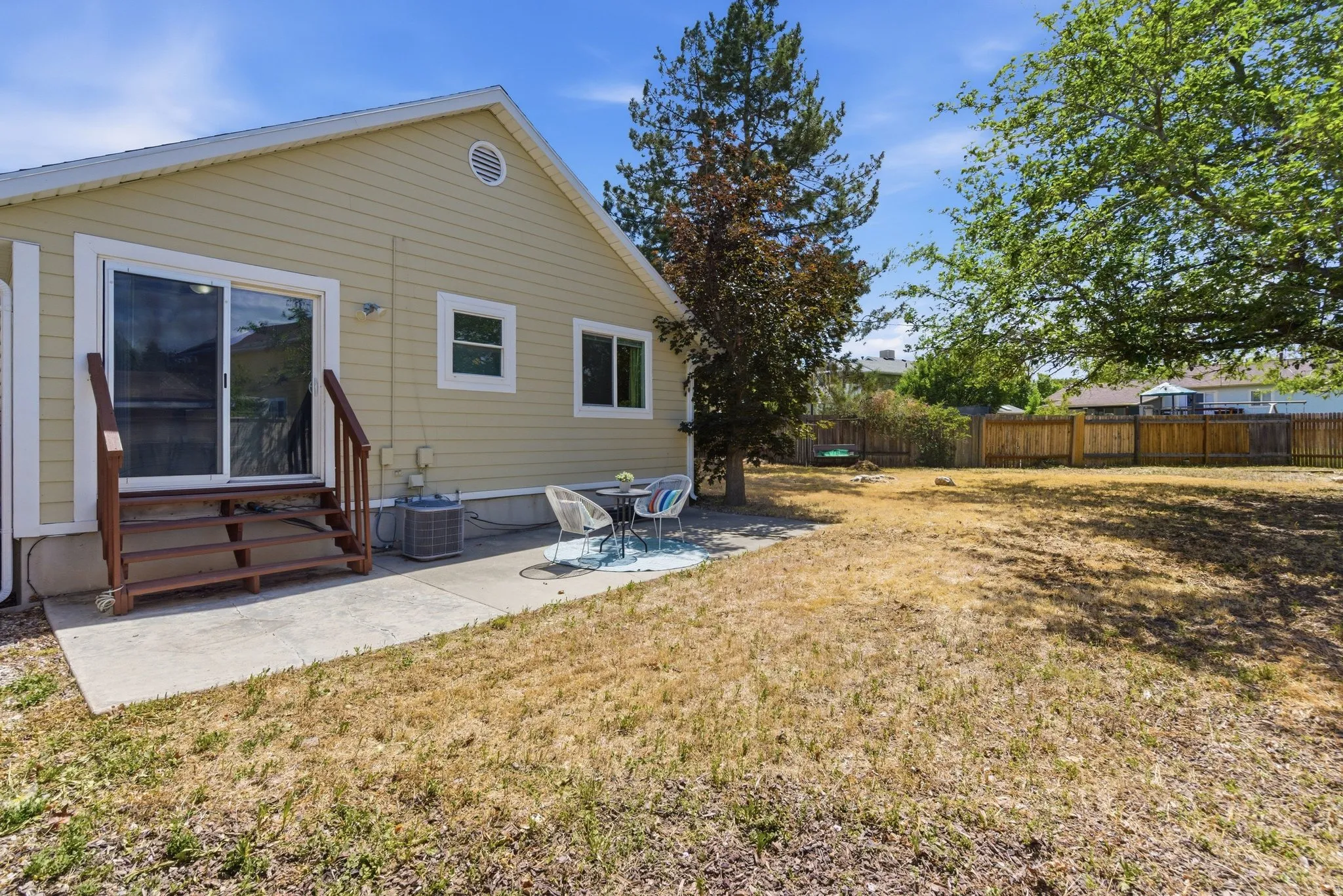 Spacious backyard featuring a concrete patio, sliding glass door access, exterior siding, and a wooden fence