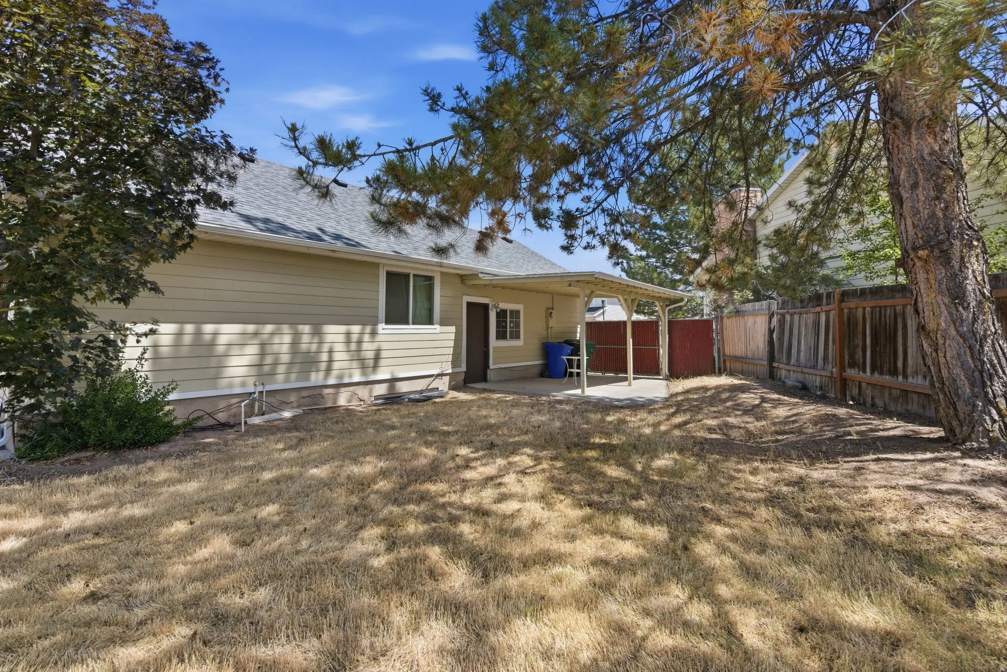 Spacious backyard featuring a covered patio, perimeter fencing, and mature trees providing natural shade