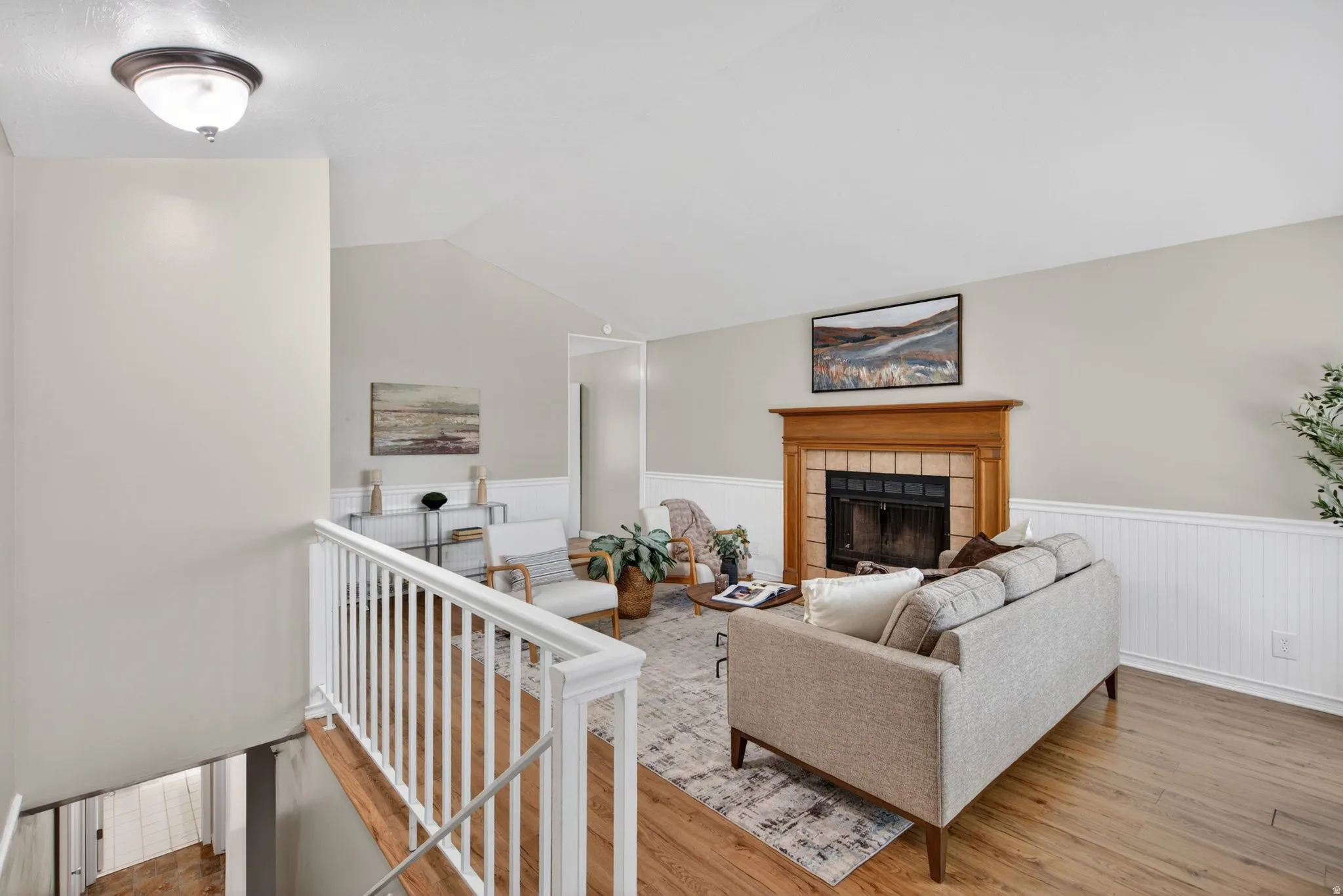 Living area featuring wood-finish flooring, a white railing, and a fireplace with a wood mantel and tile surround