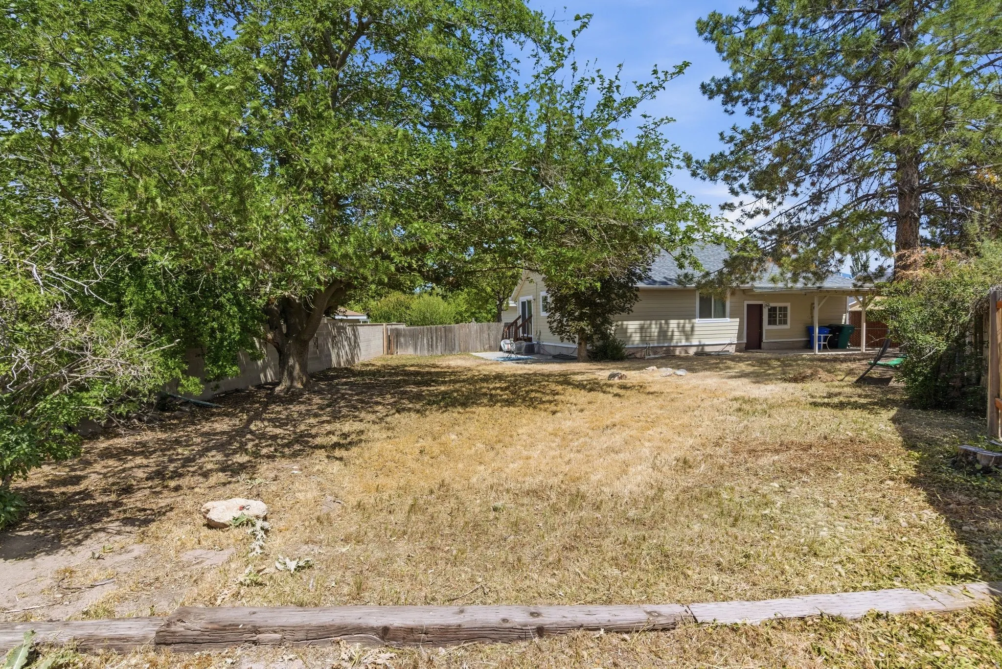 Spacious backyard featuring a large shade tree, wood fencing, and a rear exterior with siding and a covered patio area