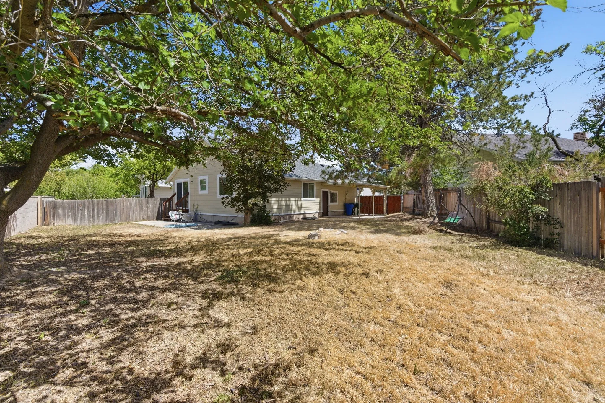 Expansive backyard featuring mature shade trees, a wooden privacy fence, and a neutral-toned exterior with a rear patio