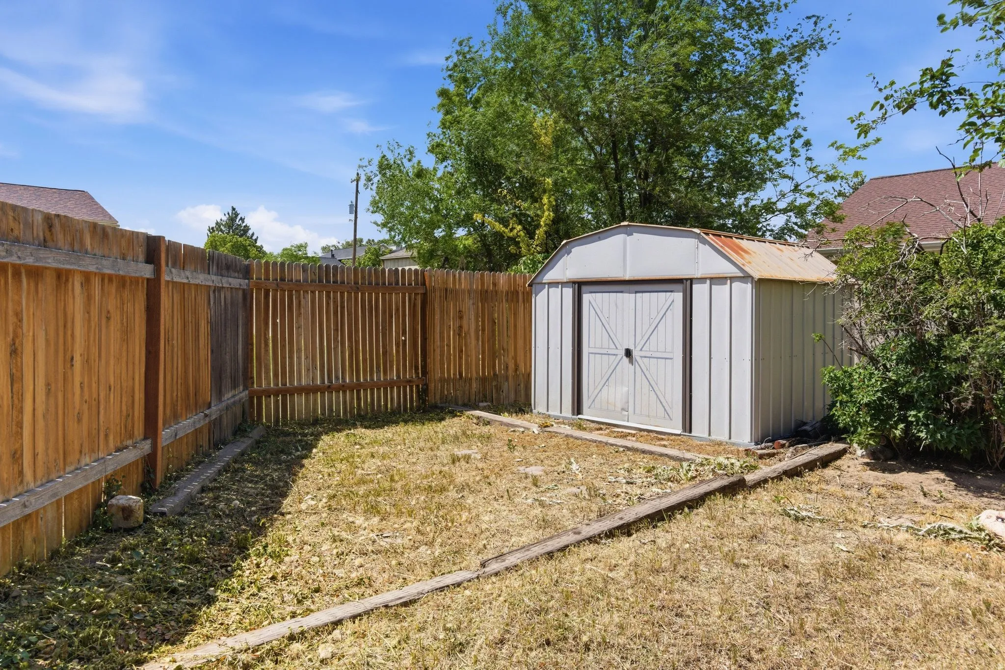 Backyard storage shed with double doors, wood privacy fencing, and surrounding mature trees