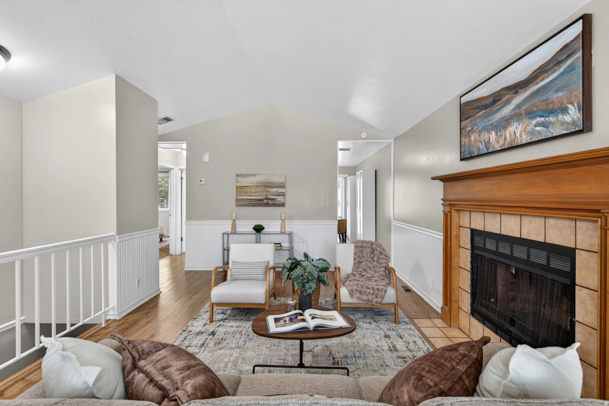Living area featuring vaulted ceilings, wood-finish flooring, and white wainscoting
