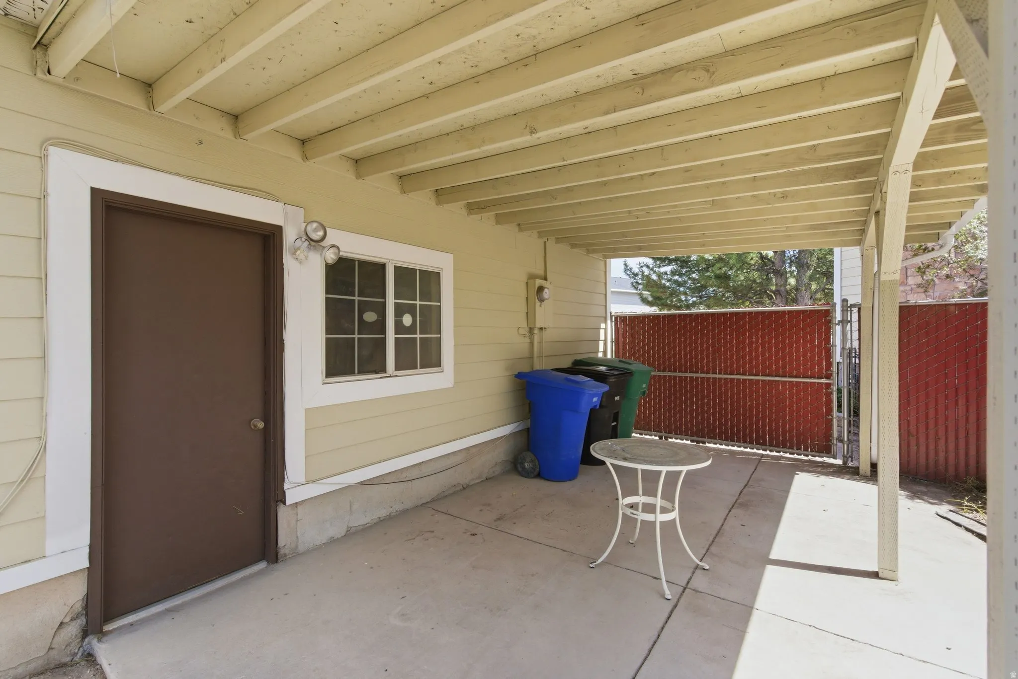 Covered patio area featuring a concrete slab, exposed beam ceiling, exterior wall siding, and privacy fencing