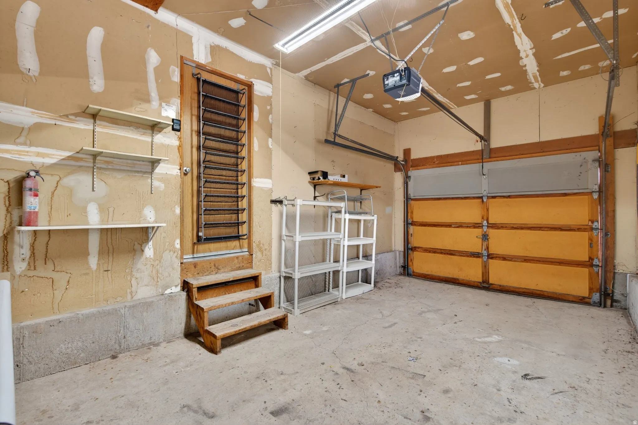 Spacious garage featuring a concrete floor, overhead lighting, and a single wood-panel garage door with an automatic opener