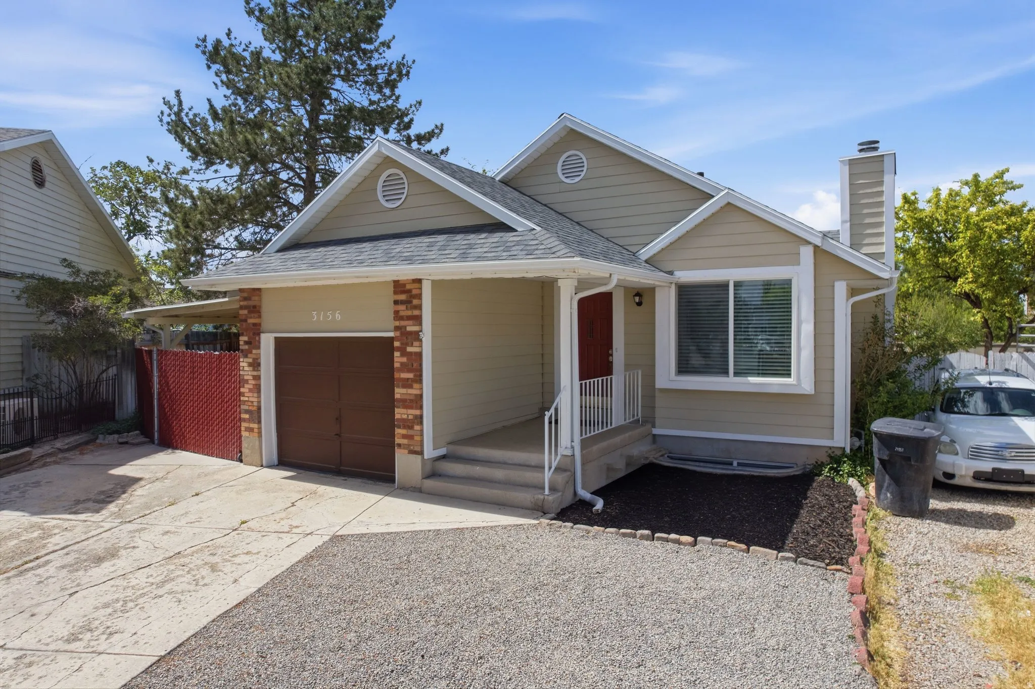 Contemporary residence featuring neutral siding, a prominent front entry with a red door, a single-car garage with brick accents, white railing, and a neat mulched garden bed