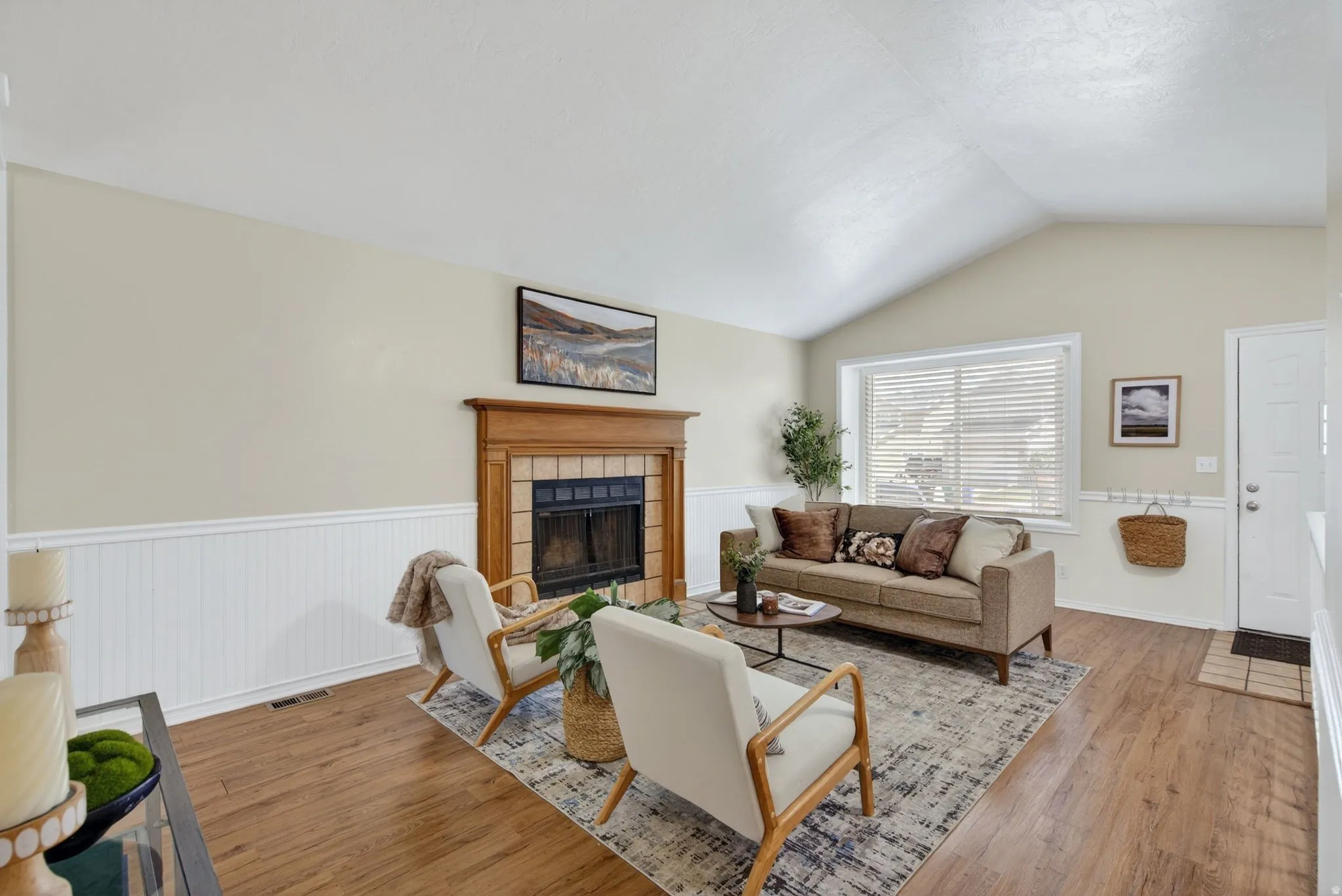 Living area featuring a vaulted ceiling, wood-finish flooring, and wainscoting