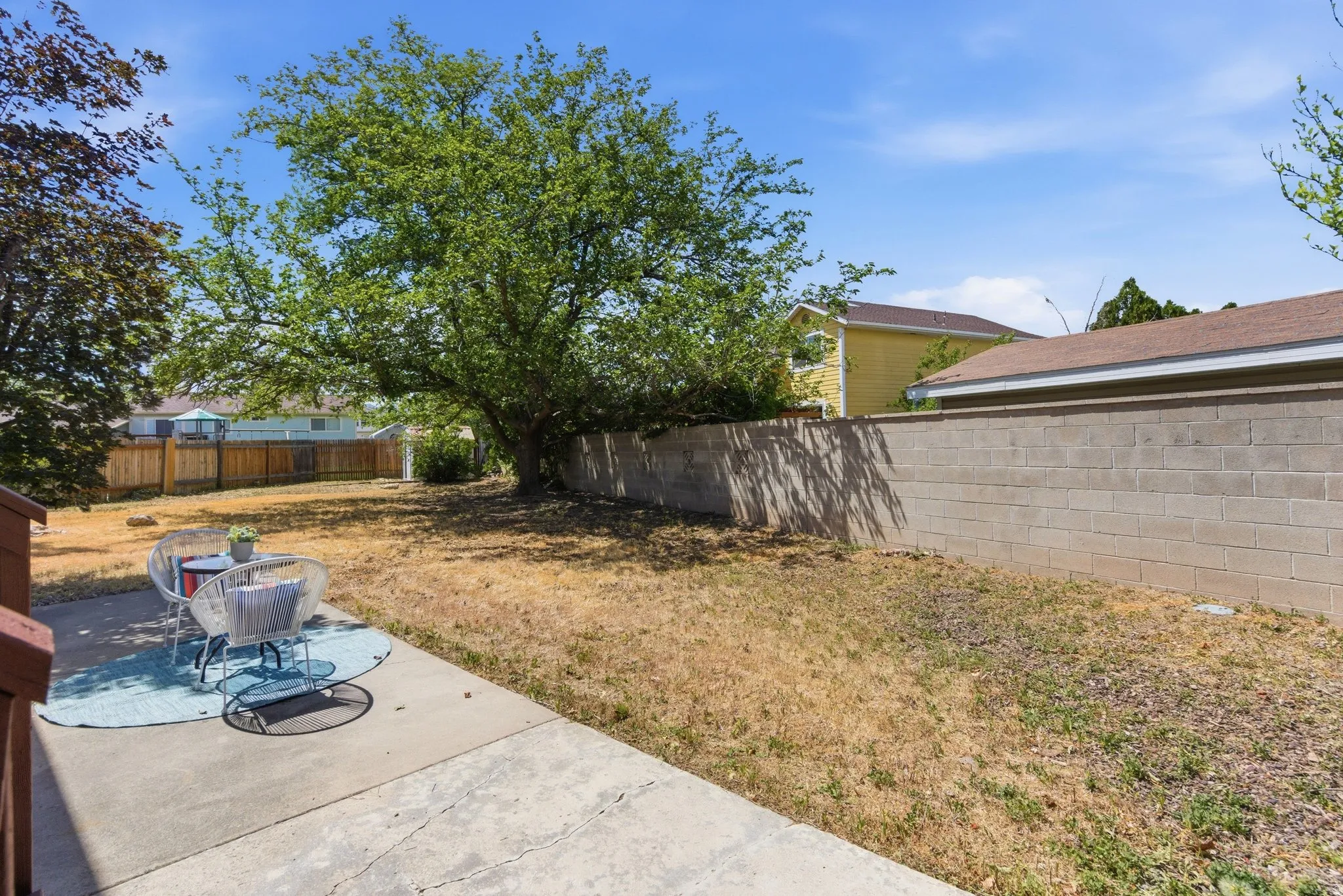 Expansive backyard featuring a concrete patio, mature trees, and a wooden privacy fence