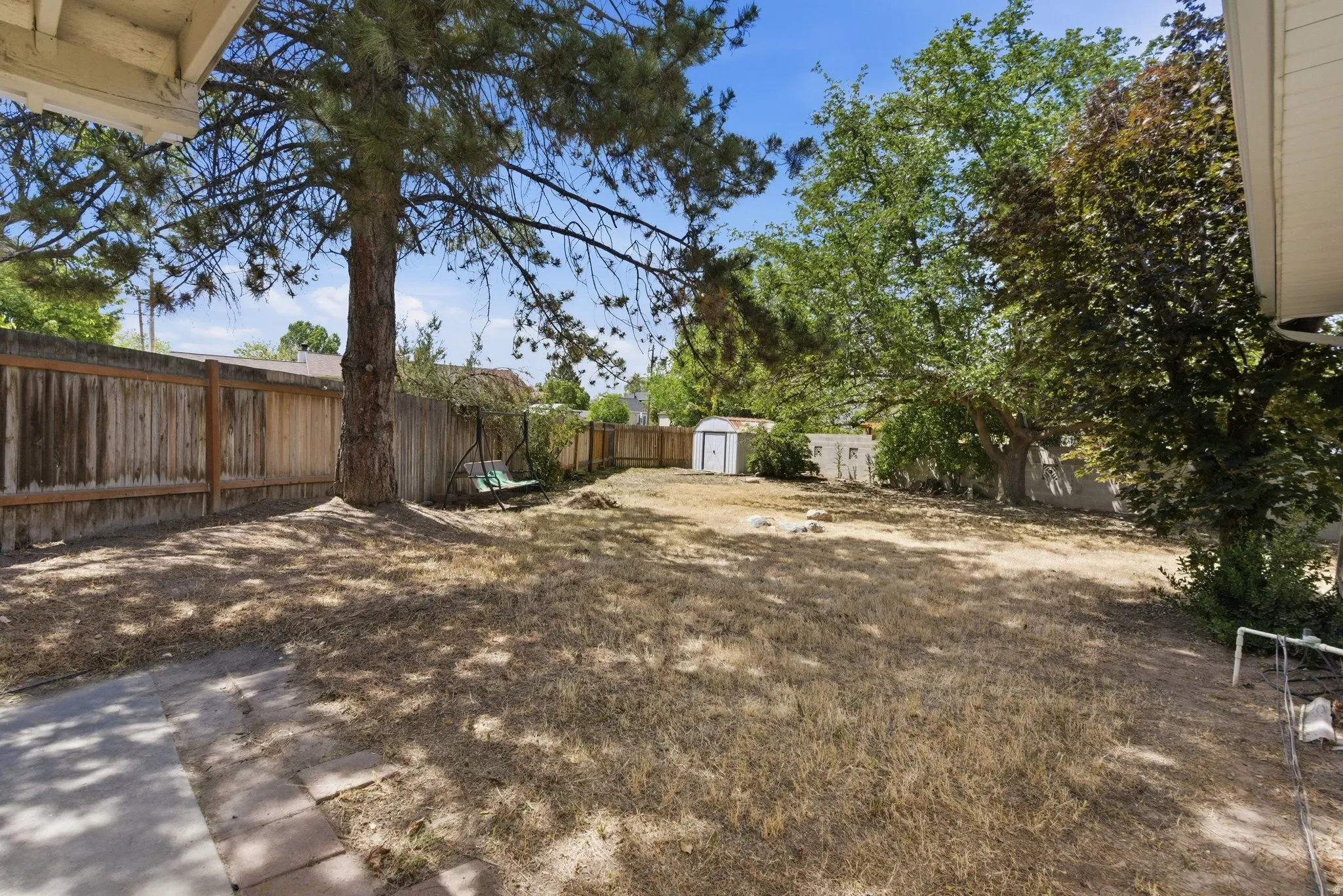 Expansive backyard featuring mature trees, a wood privacy fence, and a white storage shed