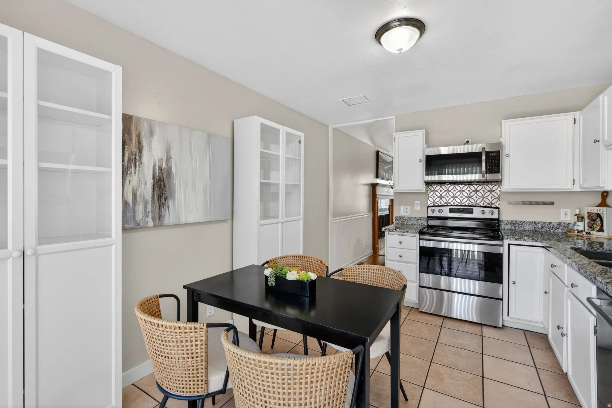 Kitchen area featuring tile flooring, white cabinetry, granite-style countertops, stainless steel appliances, and an ornamental backsplash