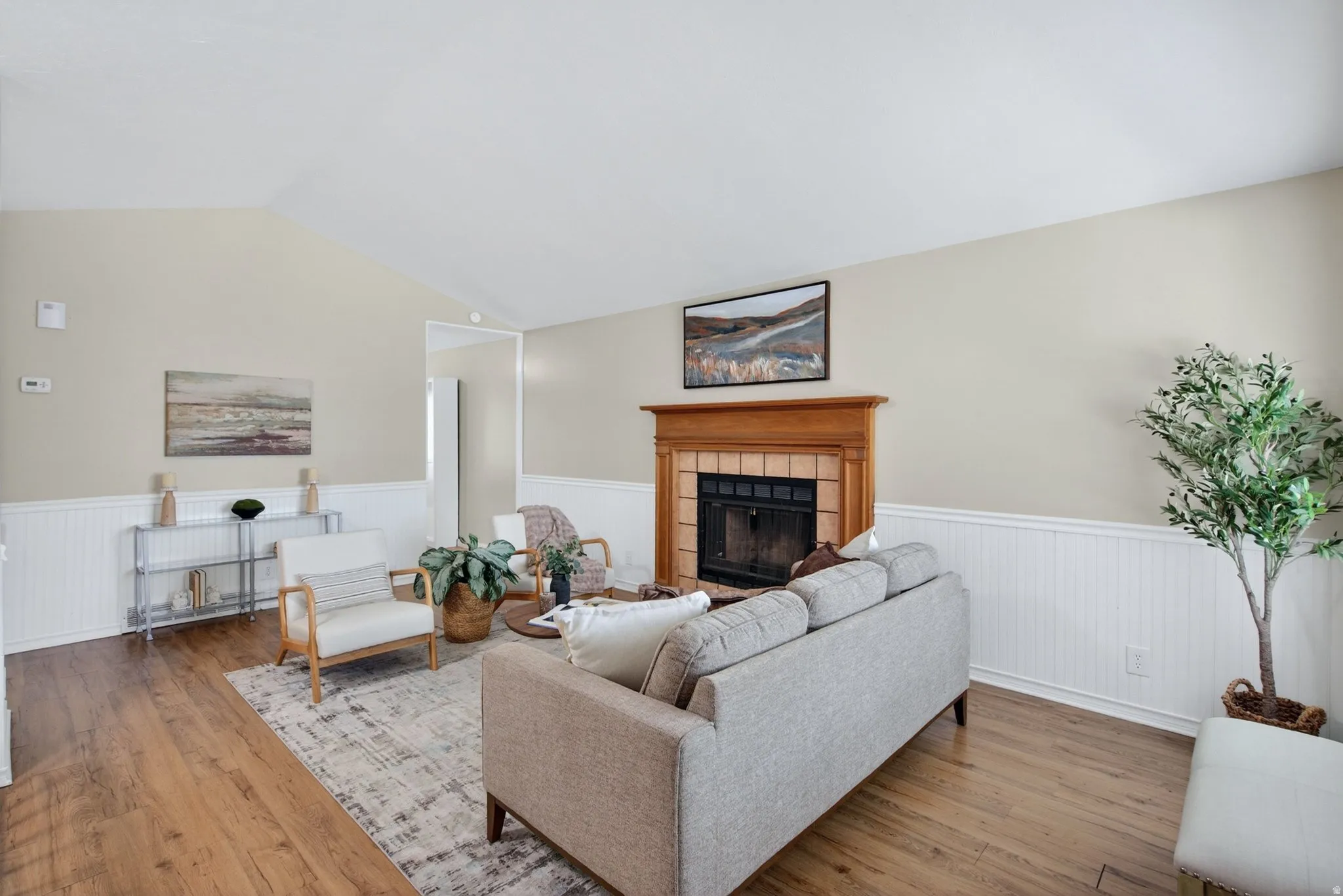 Living room featuring a prominent fireplace with a wood mantel, wood-finish flooring, and vaulted ceilings