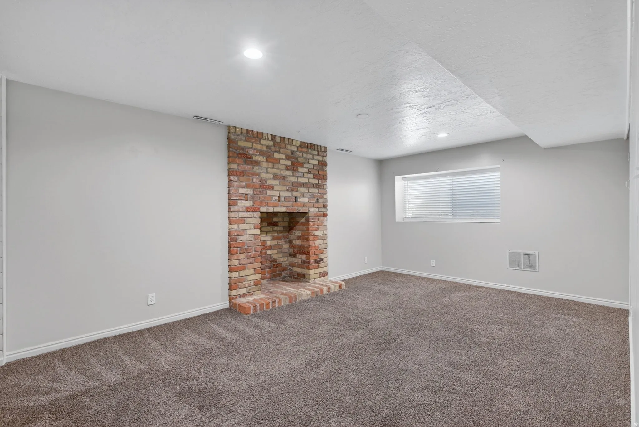 Spacious room featuring a brick fireplace, gray wall paint, and recessed lighting