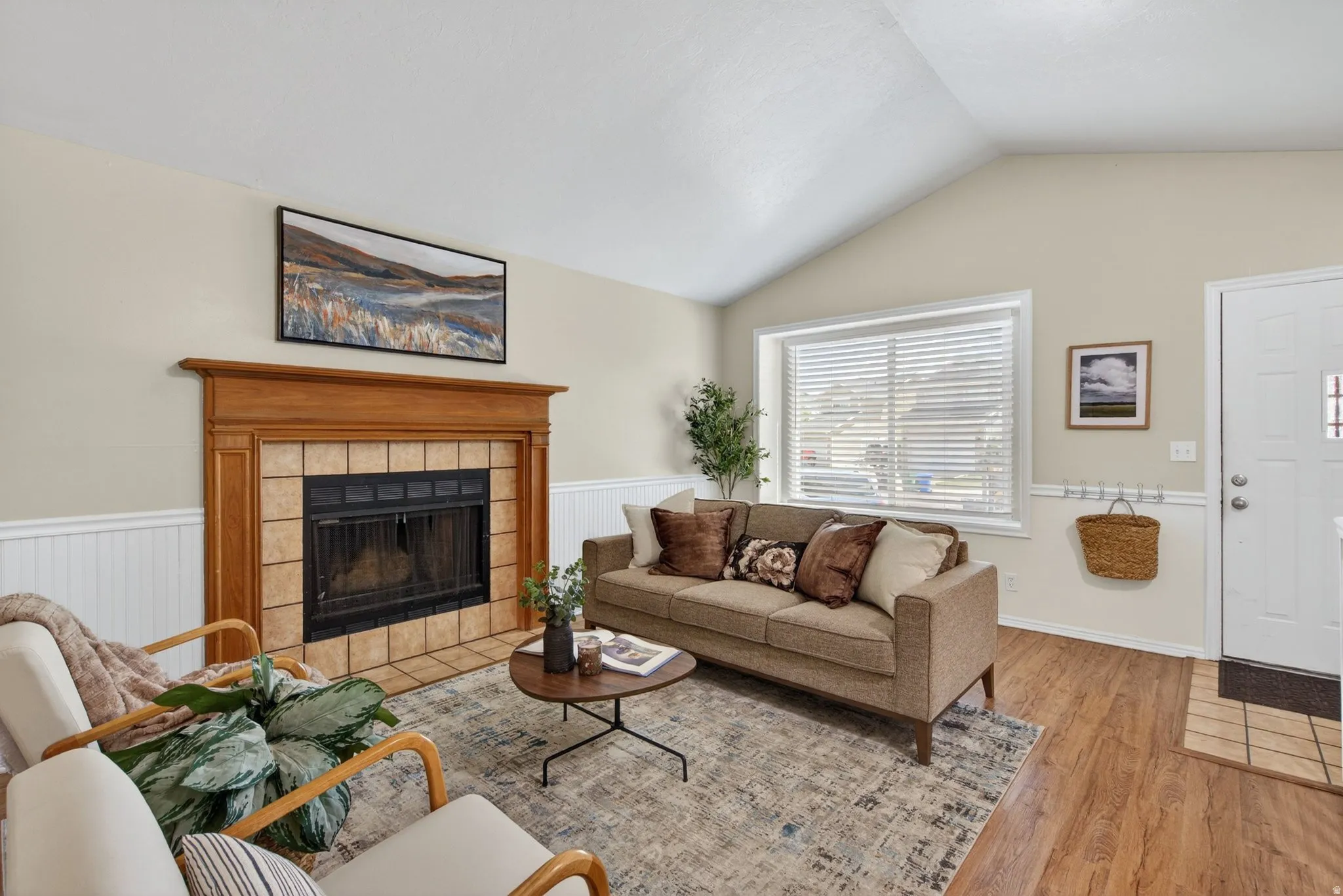 Vaulted ceiling living area featuring a wood-finish floor and a fireplace with a wood mantle and tile surround
