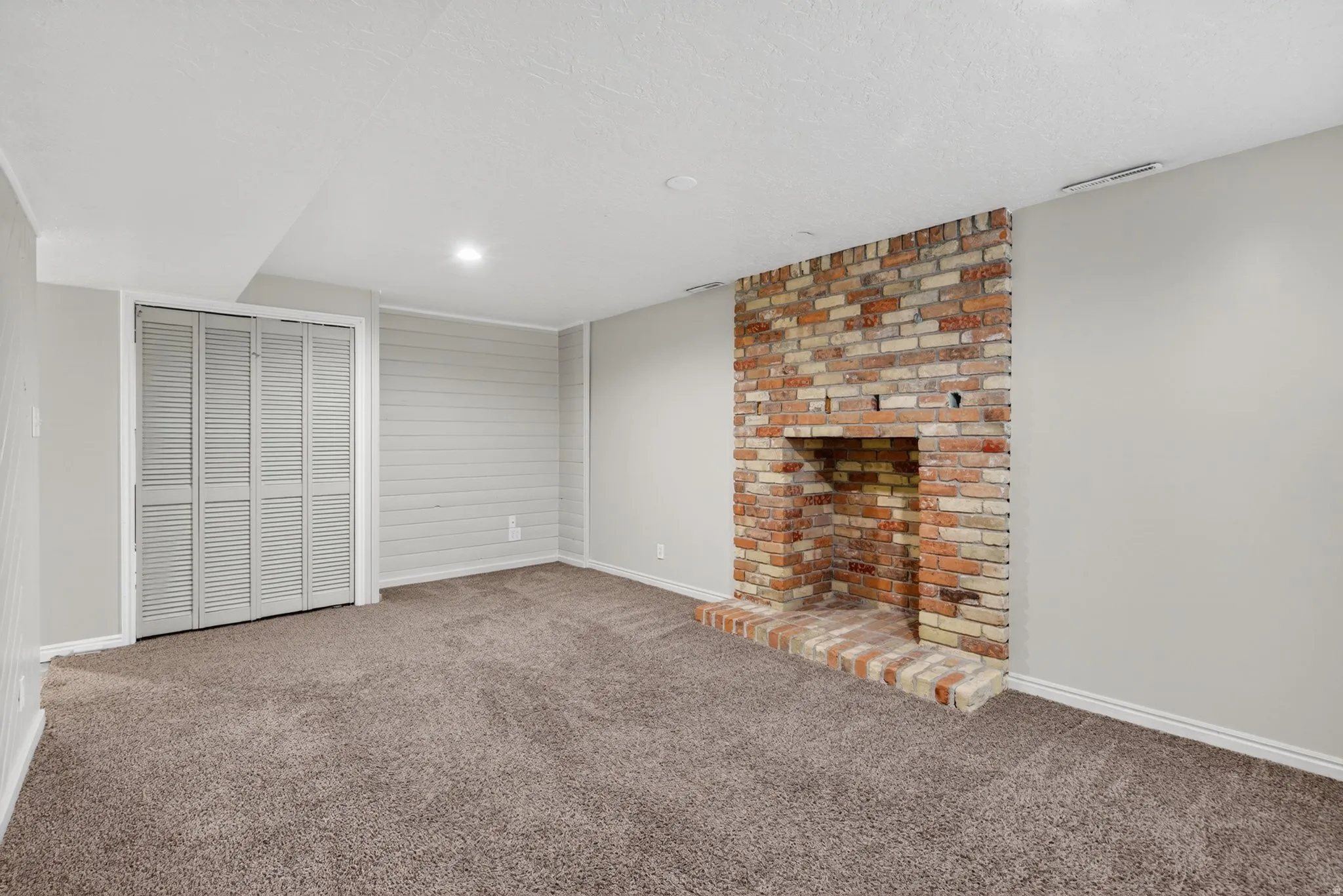 Living space featuring a brick fireplace, bifold louvered closet doors, shiplap accent wall, recessed lighting, and carpet flooring