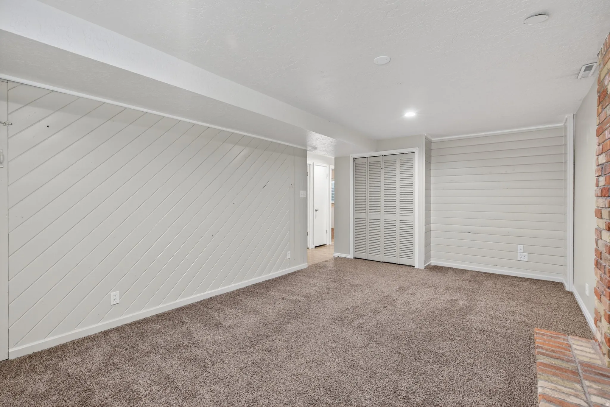 Carpeted room featuring diagonal shiplap paneling on one wall and horizontal shiplap paneling on another, with a brick accent wall