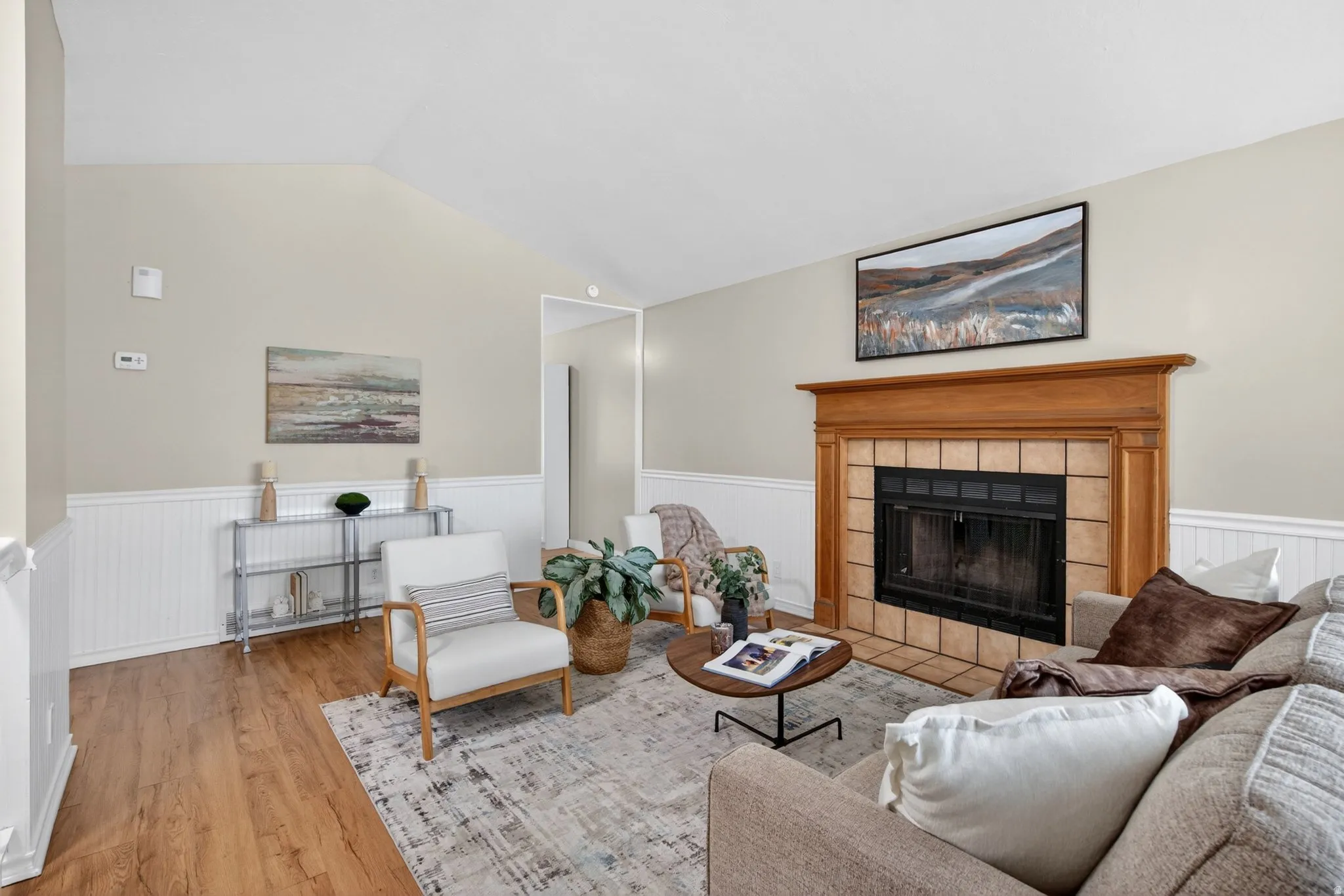 Living space featuring a wood-finish flooring, vaulted ceiling, and wainscoting