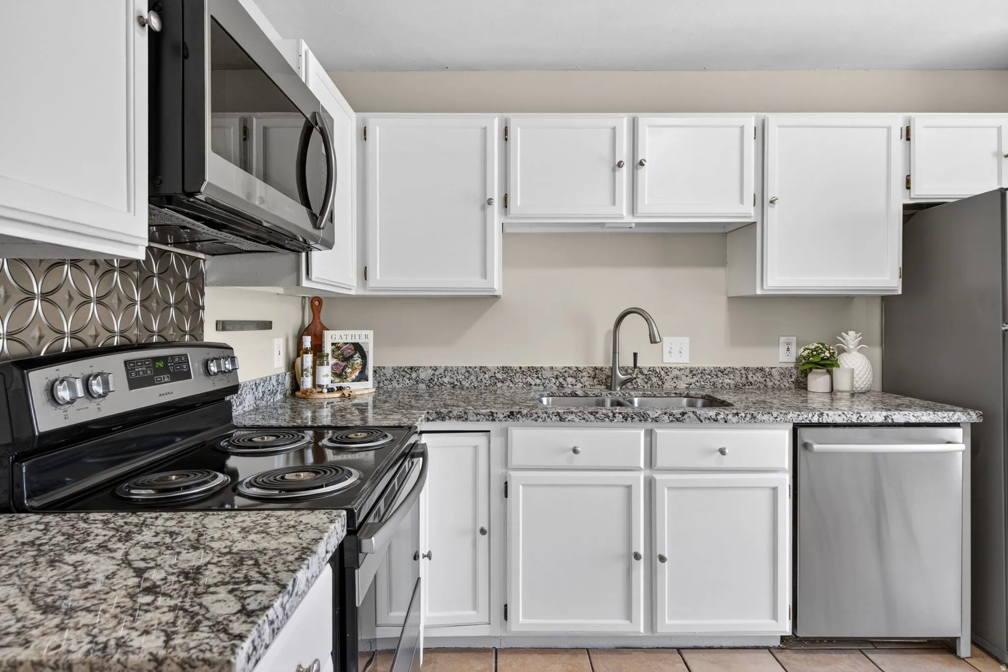 Kitchen featuring white cabinetry with silver hardware, speckled countertops, a stainless steel dishwasher, and a black electric range with an overhead microwave
