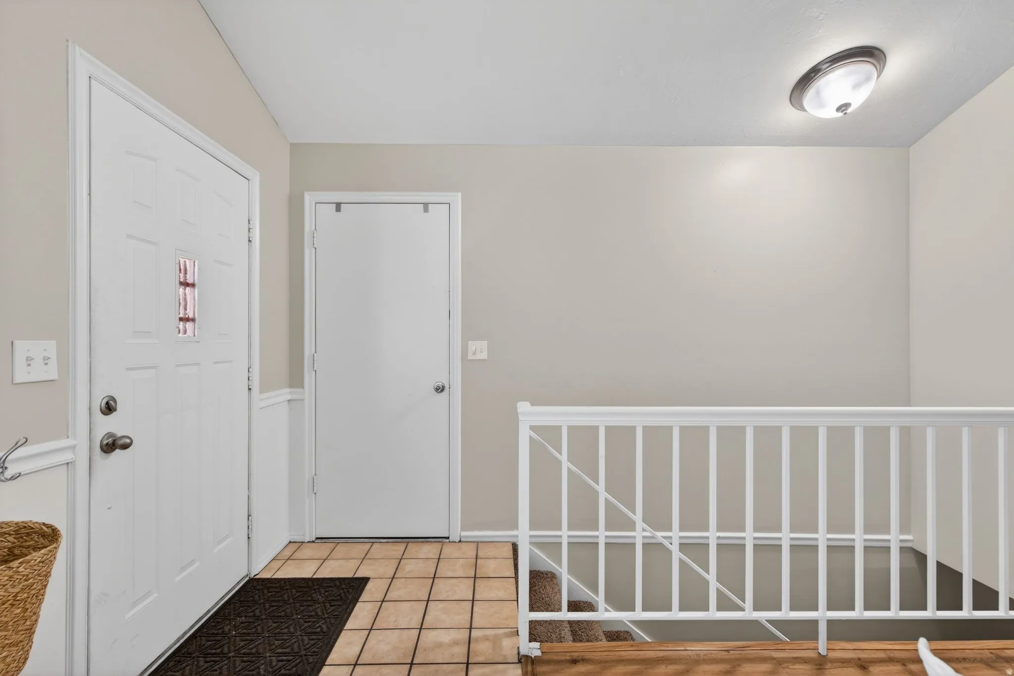 Entryway featuring neutral wall paint, tile flooring, a white paneled door with a window insert, and a white staircase railing