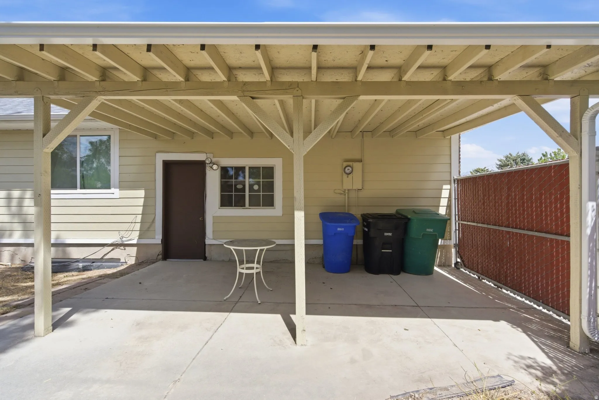 Concrete patio with a light-colored wood-frame overhang, featuring access to the property and a privacy fence