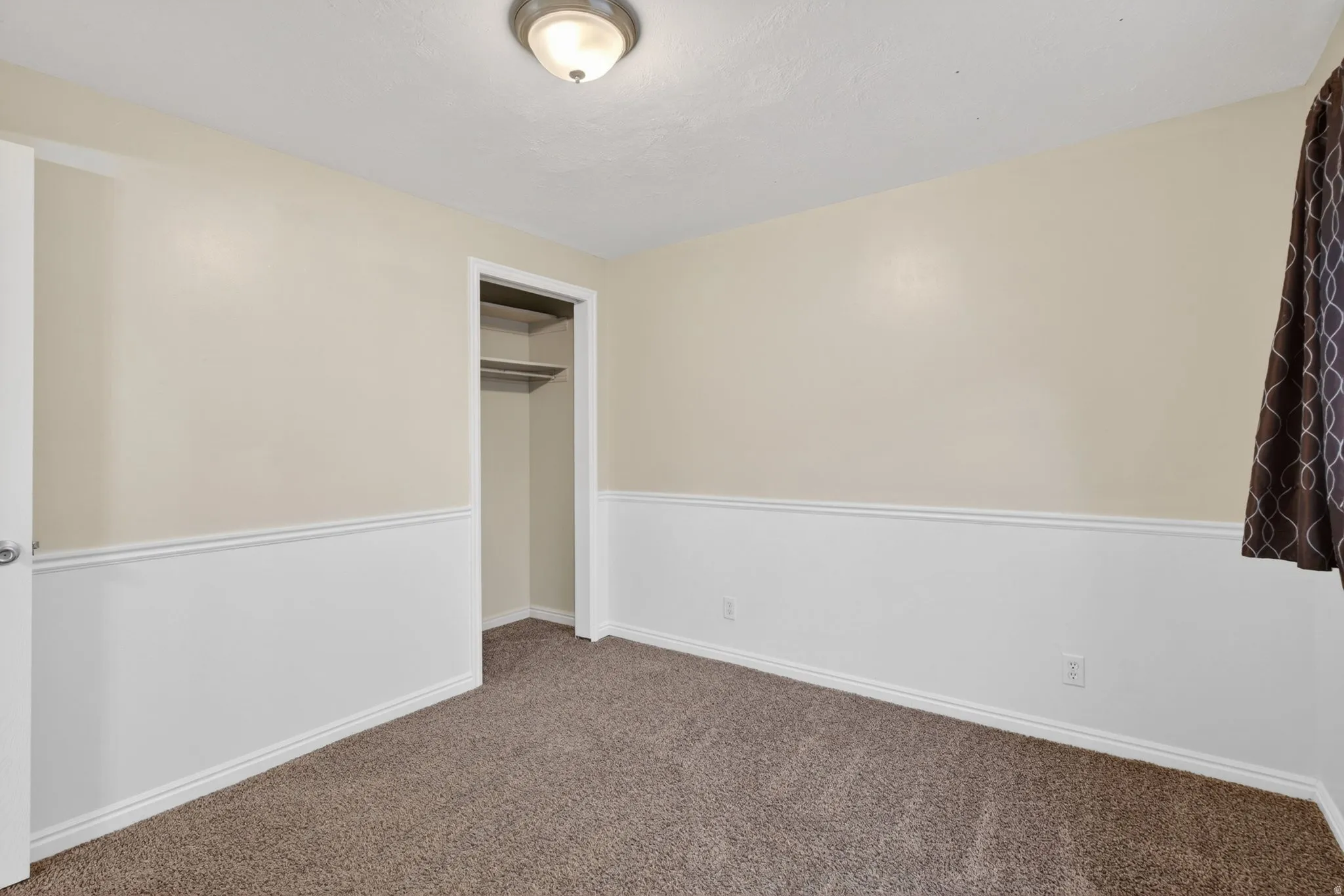 Carpeted room featuring a ceiling-mounted light fixture, two-tone painted walls with wainscoting, and a closet with built-in shelving