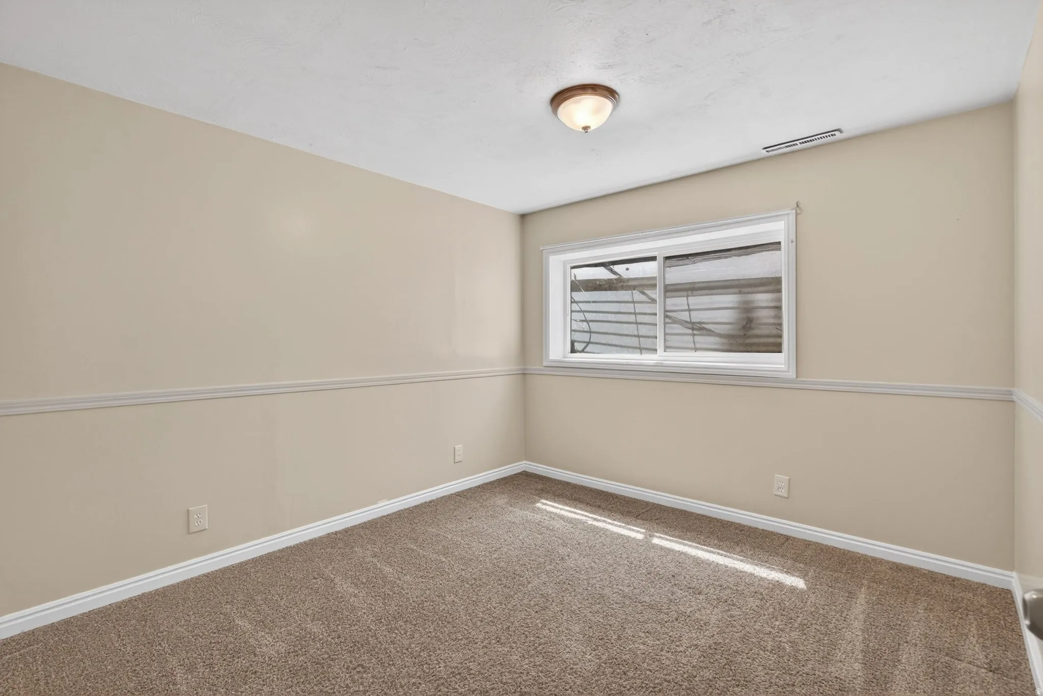 Neutral tone wall paint, textured carpet flooring, baseboard trim, chair rail molding, and a single window with a white frame
