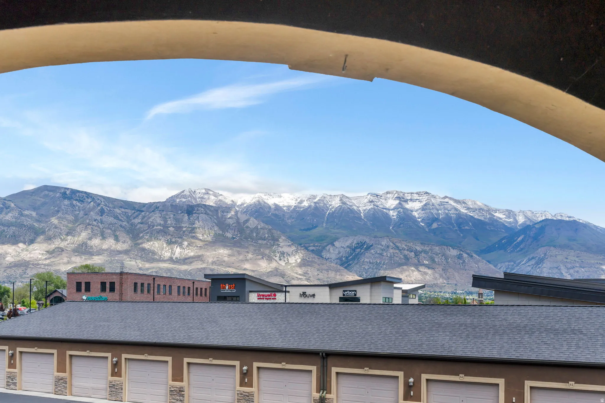 Distant snow-capped mountains frame a residential and commercial area, featuring a row of garages with stone accents and a shingled roof
