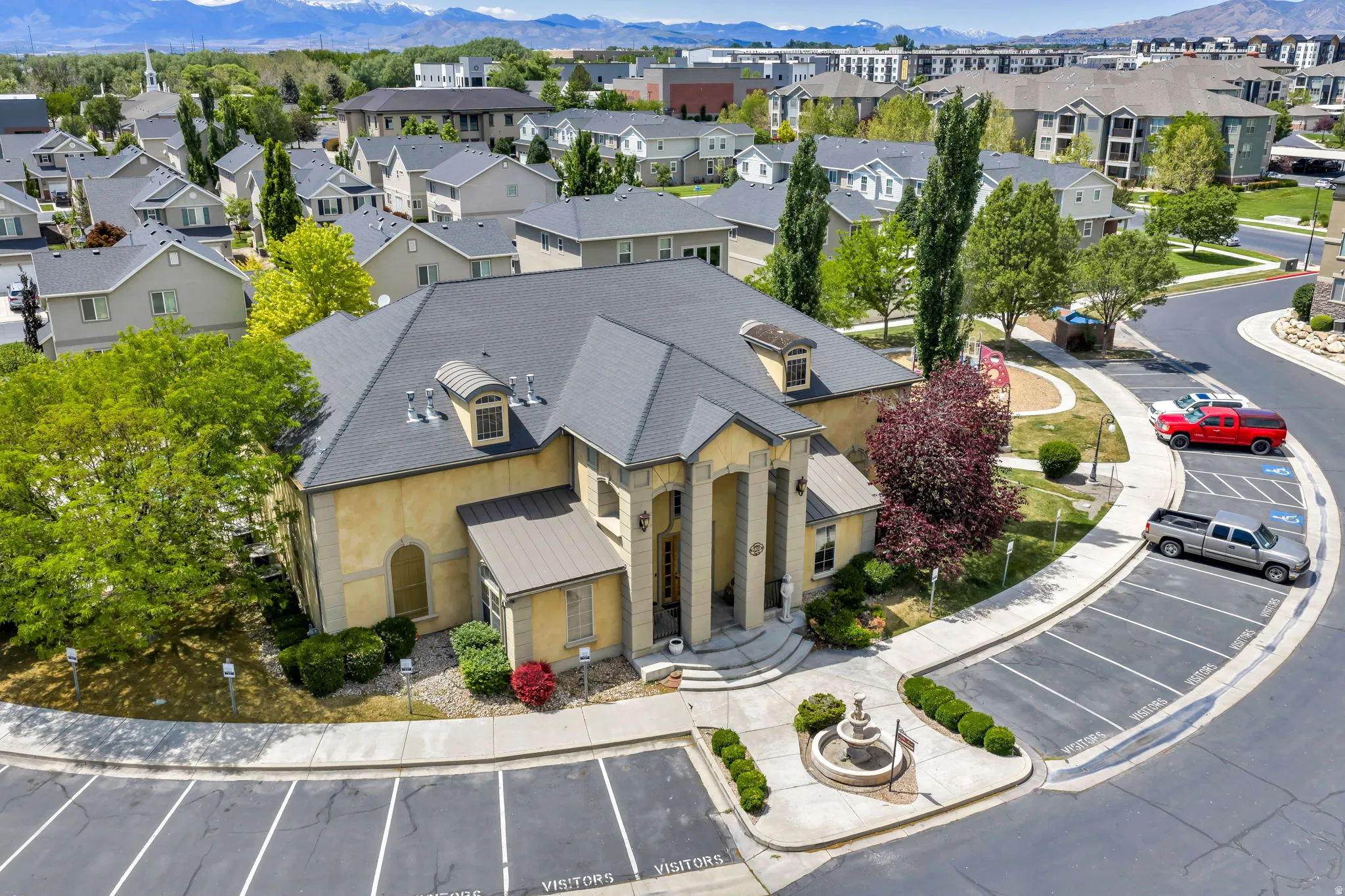 Stucco-sided building featuring a prominent portico entrance with columns, dormer windows, and a dark gray shingle roof