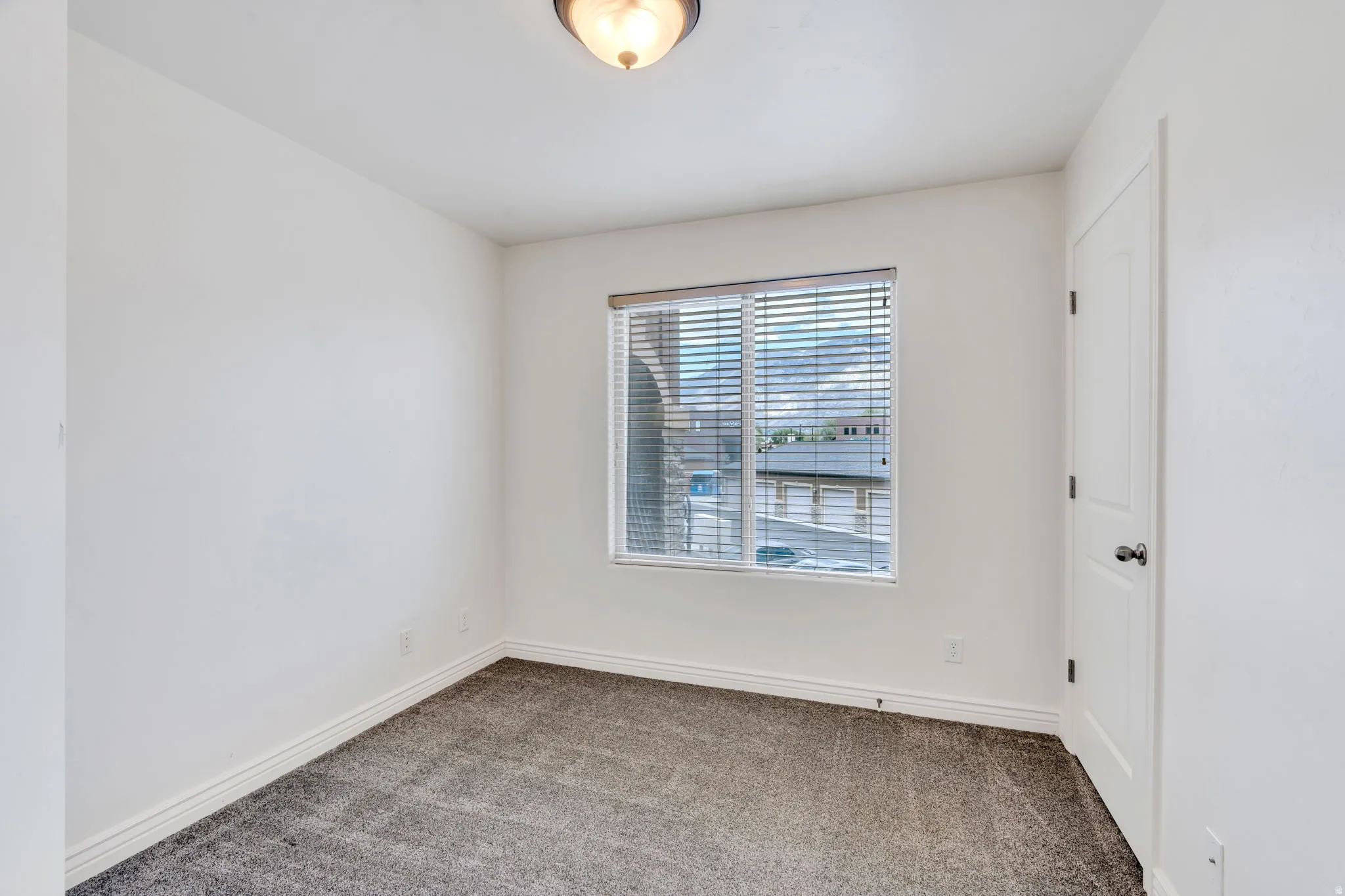 Room featuring a window with blinds, a ceiling-mounted light fixture, white walls, and gray carpet