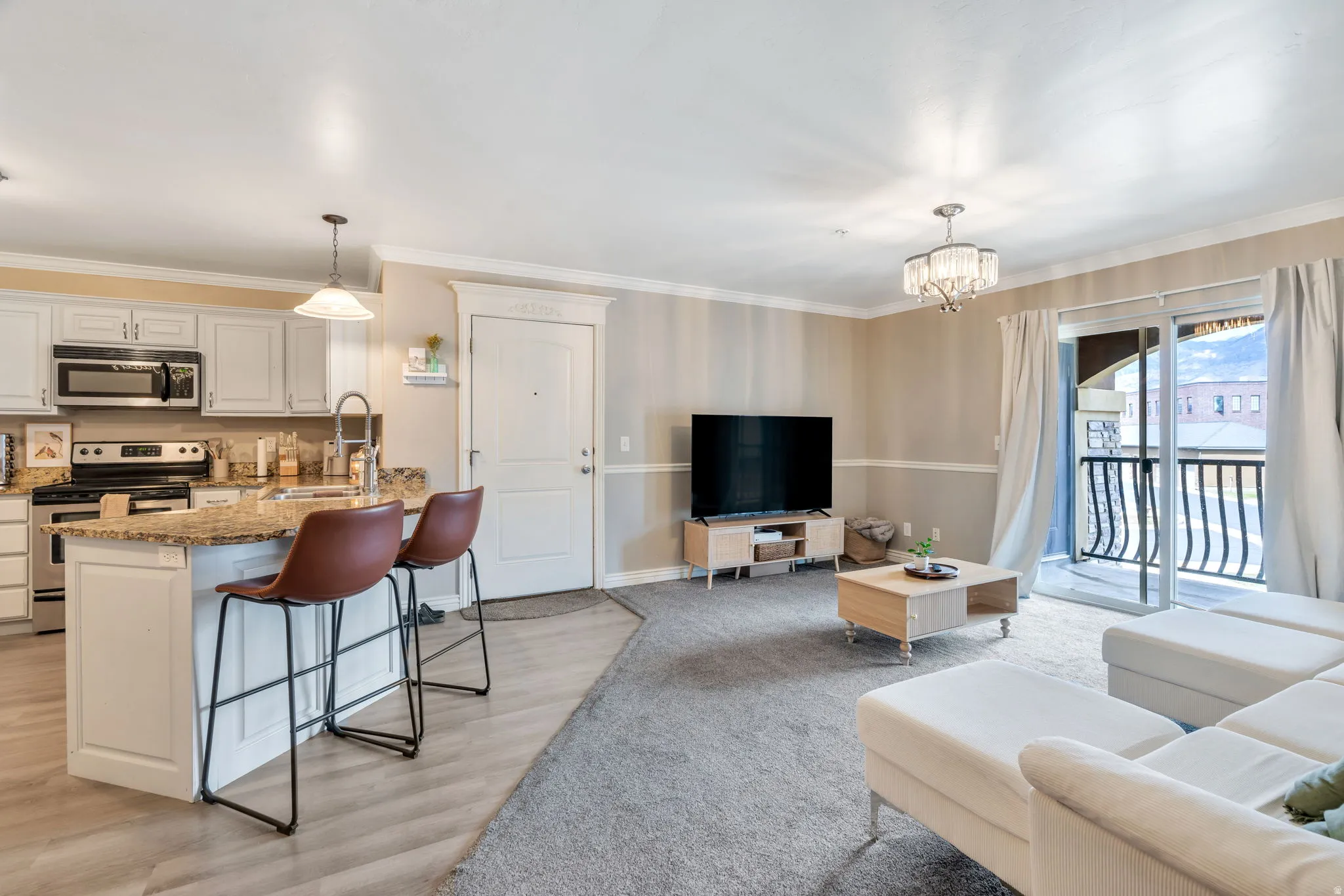 Open-concept living space featuring a kitchen island with stone countertop, stainless steel appliances, wood-finish flooring, and a private balcony