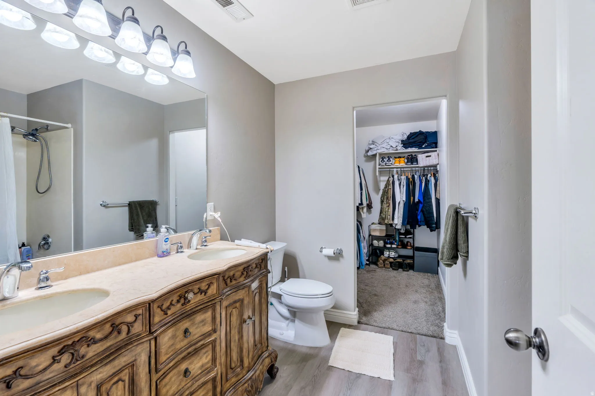 Bathroom featuring a dual-sink vanity with an ornate wood-finish base, a large mirror, and an overhead light fixture