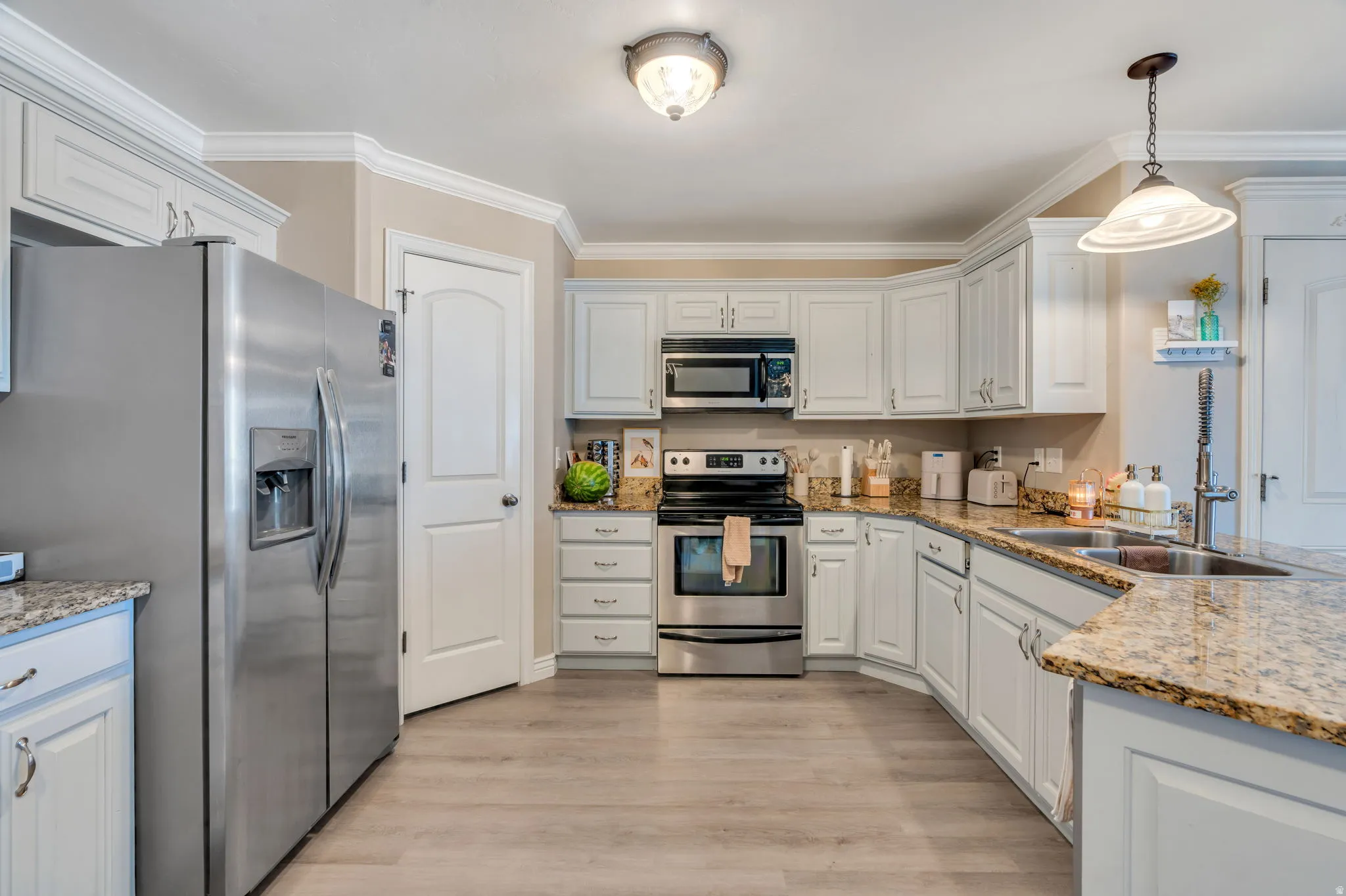 Kitchen featuring light wood-finish flooring, white cabinetry with crown molding, stainless steel appliances, and stone countertops